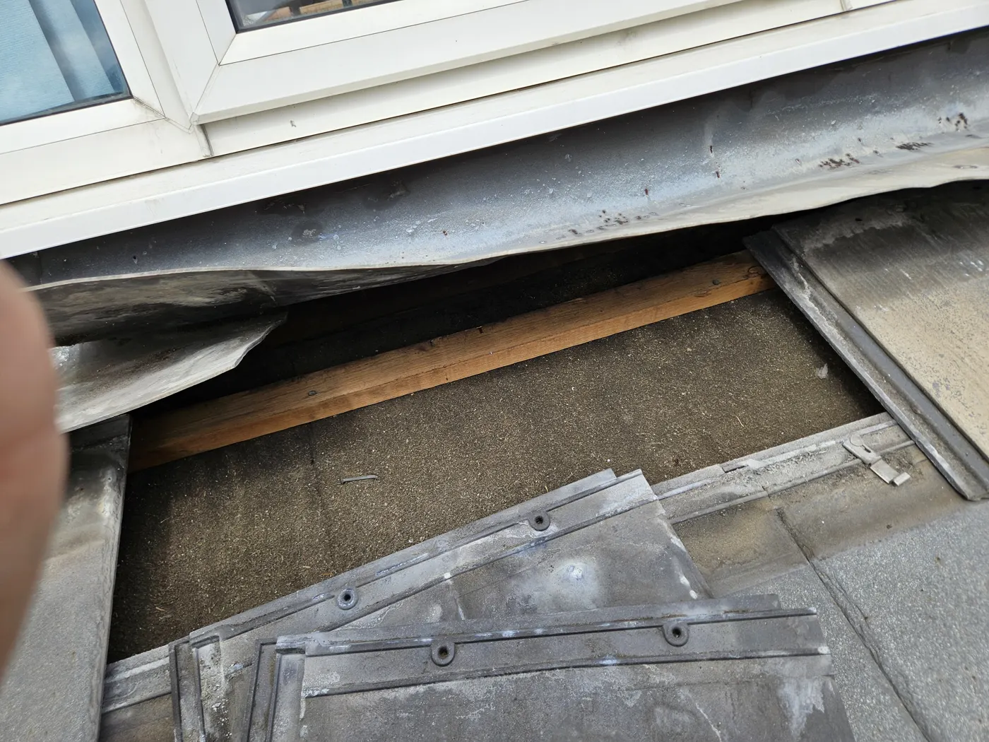 Lead flashing lifted away from under a window sill exposing the gap behind the tiles